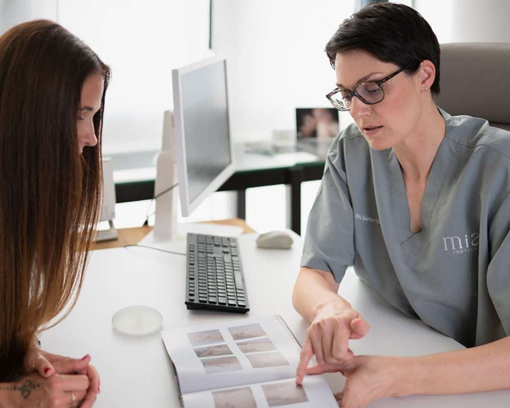Dr. med. Sabrina Hoormann erklärt einer Patientin in einem Beratungsgespräch die verschiedenen Optionen für eine Brustvergrößerung anhand eines Fotobuchs mit Ergebnissen.