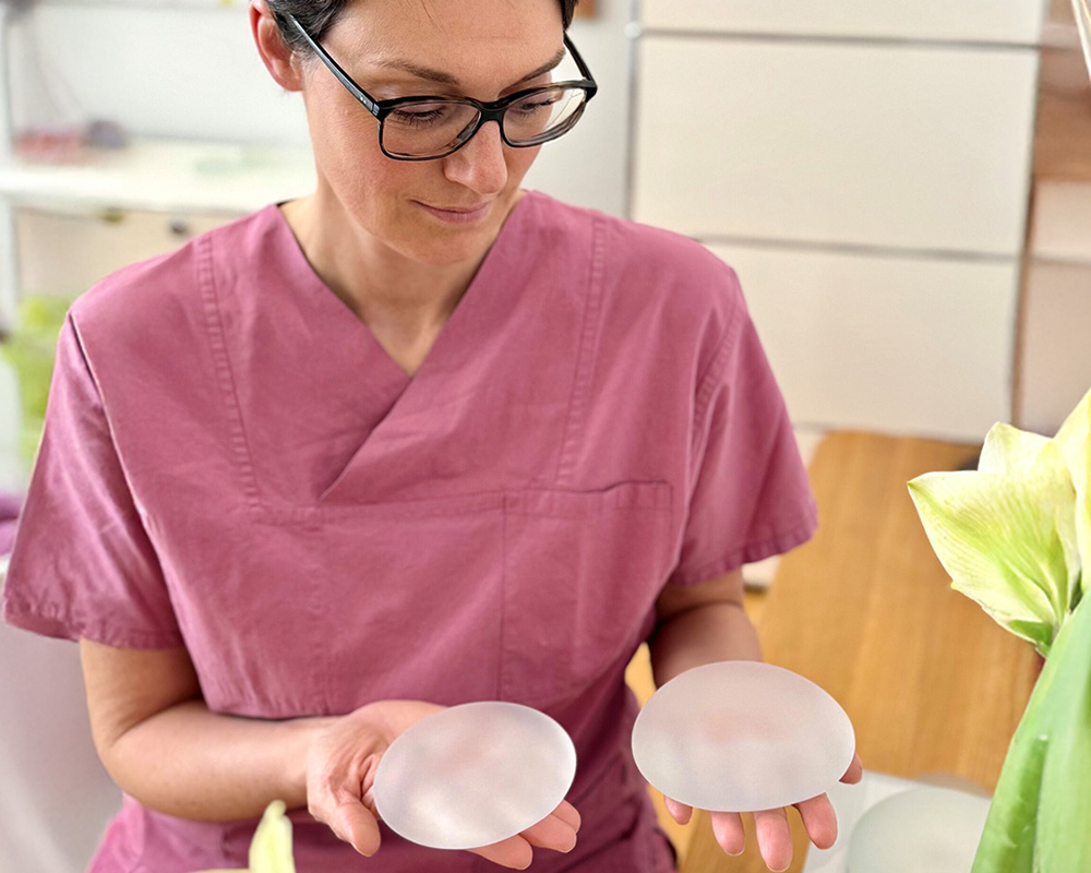 Dr. med. Sabrina Hoormann hält zwei Brustimplantate in den Händen und erklärt ihre Unterschiede als Teil der Beratung zur ambulanten Brustvergrößerung.